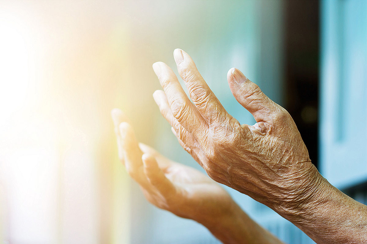 Elderly hands held palm up reaching up to warm light. Credit: Photo 78594768 © Pop Nukoonrat | Dreamstime.com