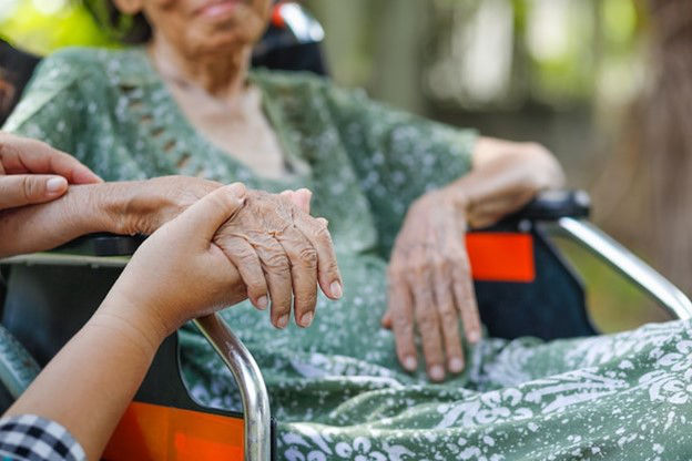 A volunteer holds the hand of an elderly woman in wheel chair