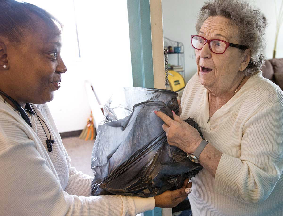 A woman volunteer hands a bag to an elderly woman who responds in surprise