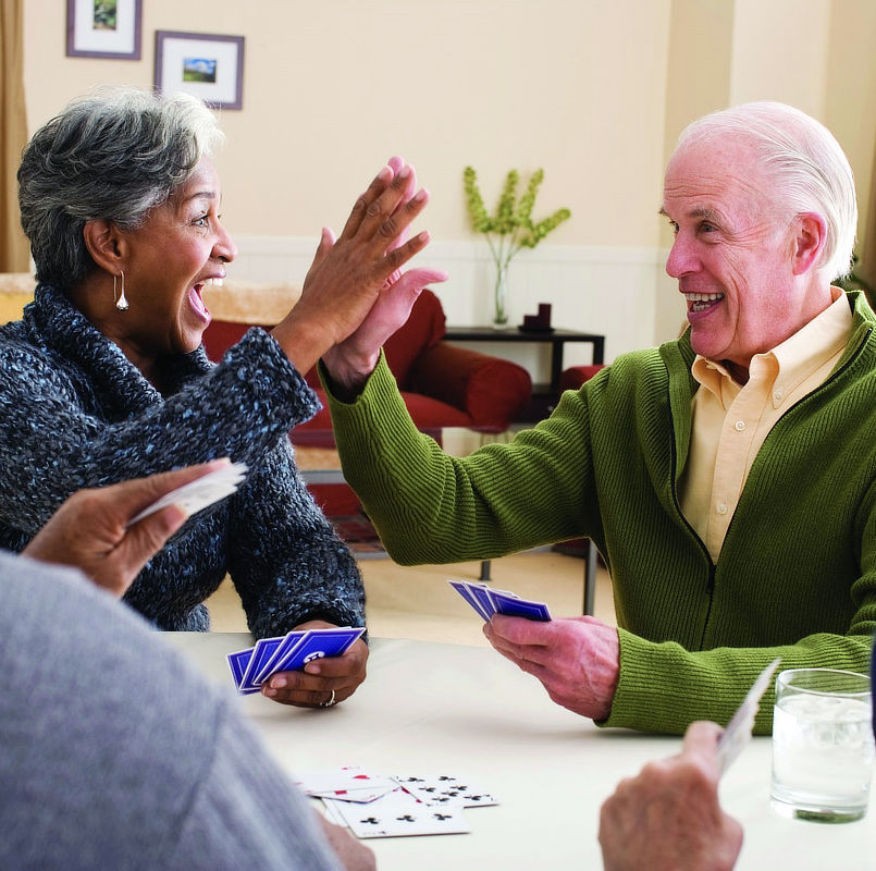 An elderly woman and man share a high fives while playing cards