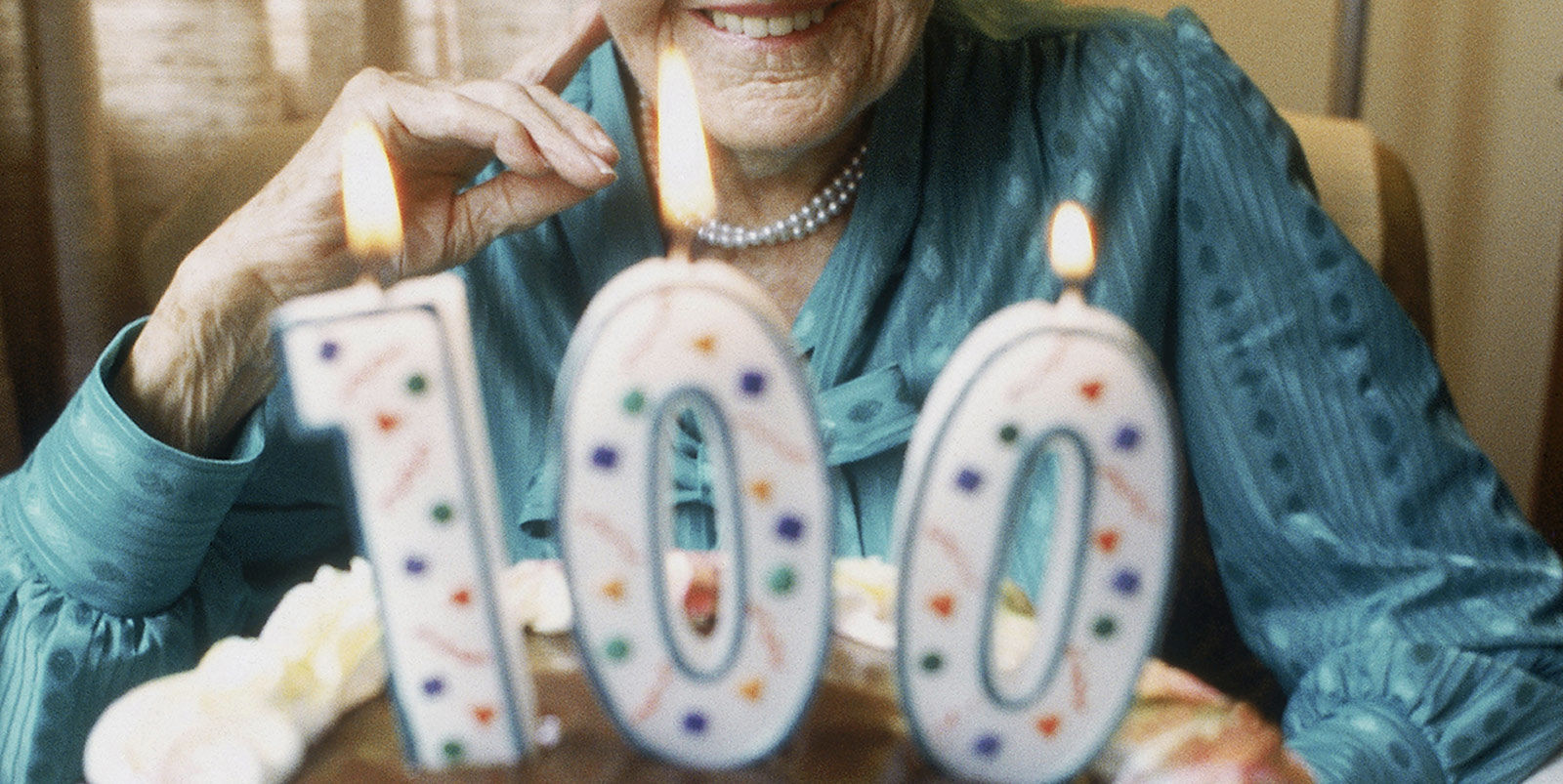 Elderly woman smiling at her birthday cake with a 100 candle on top